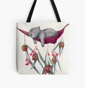 This is a tote bag with the image of a relaxing wombat in a hammock. The image is printed on both sides of the washable cloth bag. The hammock has gum leaves, nuts and flowers pinned to it. This image is painted by Patricia (PJ) Hopwood-Wade.